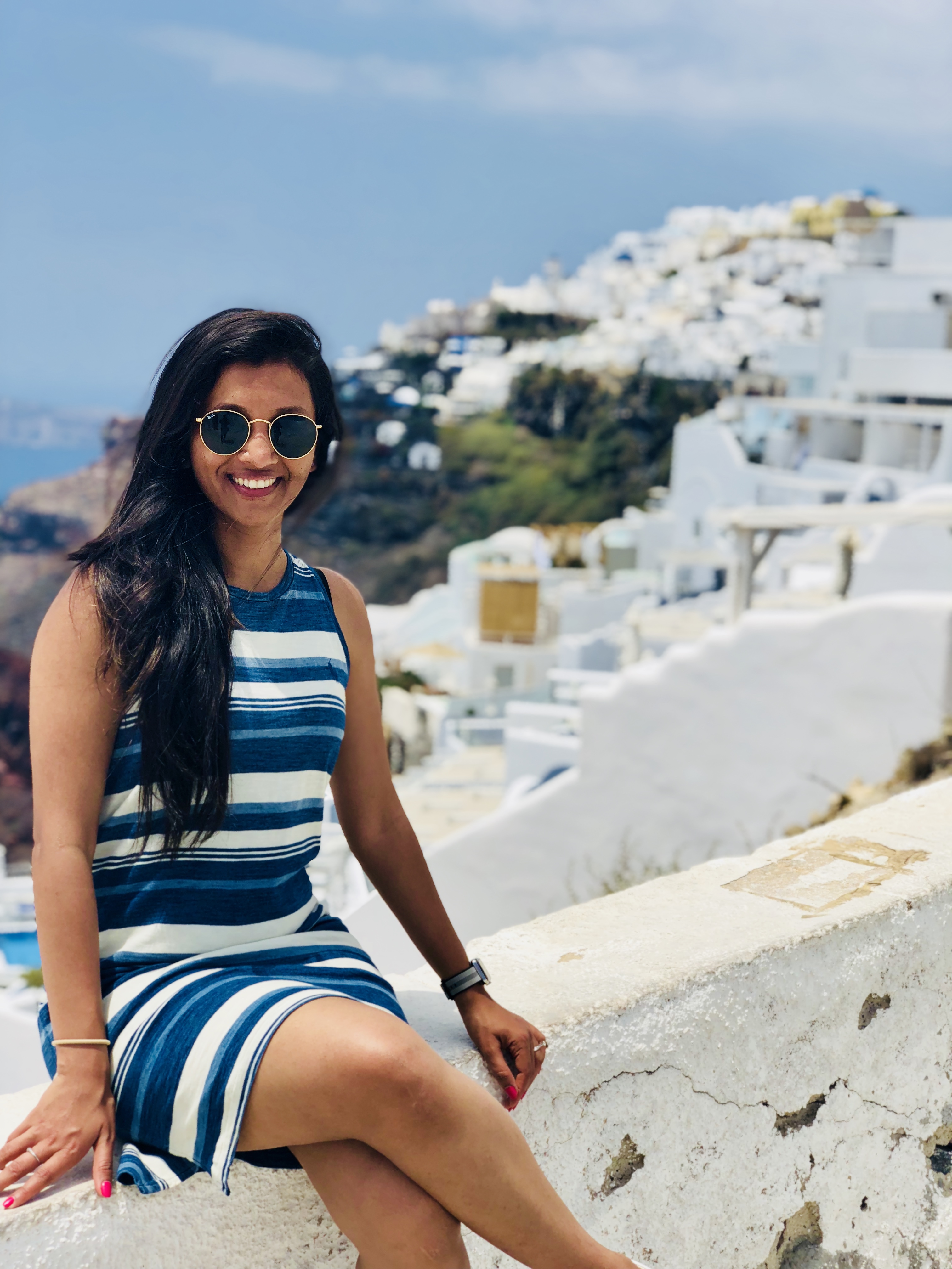 Varuna smiling in a blue and white striped dress by whitewashed buildings